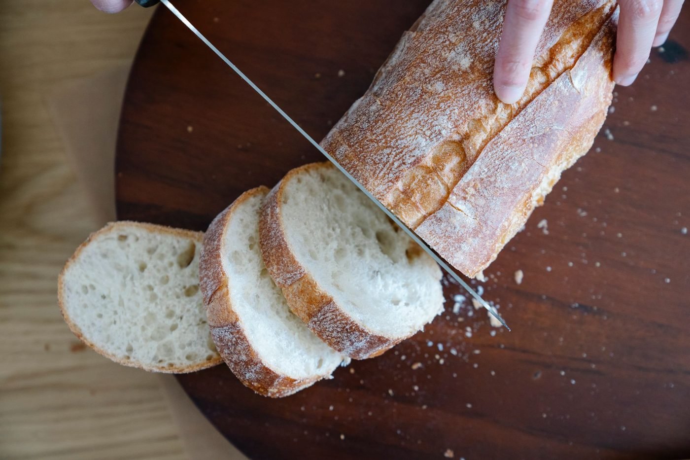 Ein Brot wird auf einem Holzbrett mit einem langen Messer in Scheiben geschnitten